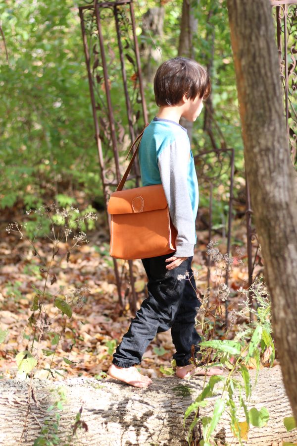 Child in the woods with his leather adventure bag.