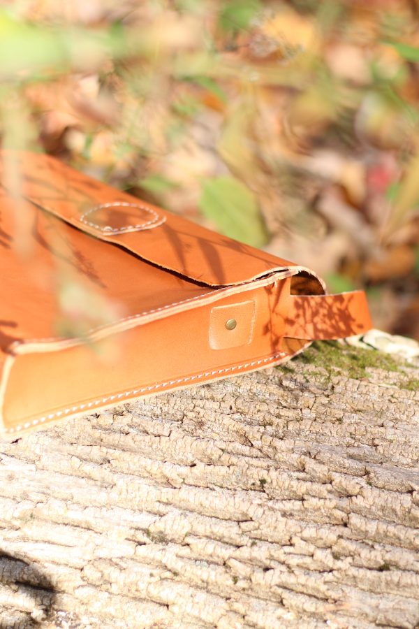 Close up of the strap insertion of a kids vegetable tanned leather satchel, on a mossy log.