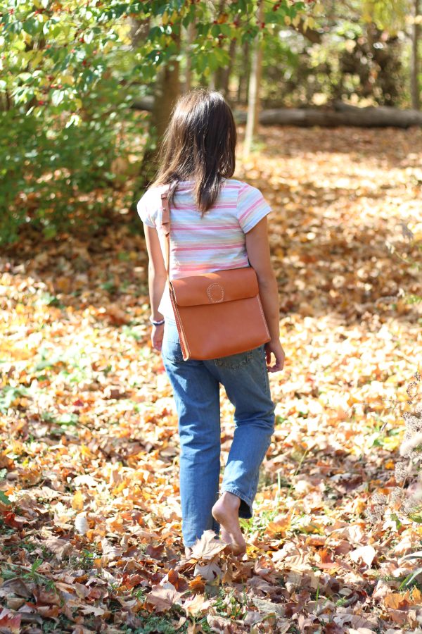 Young girls walking into the woods with her leather adventure bag.