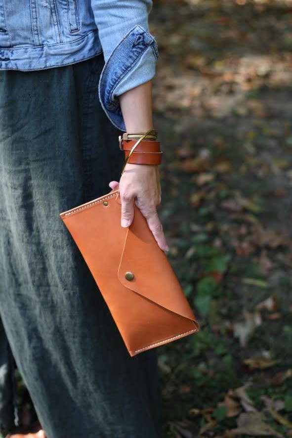 Wanderlust Leather Wristlet in Tan, held against a linen skirt and woodland floor.