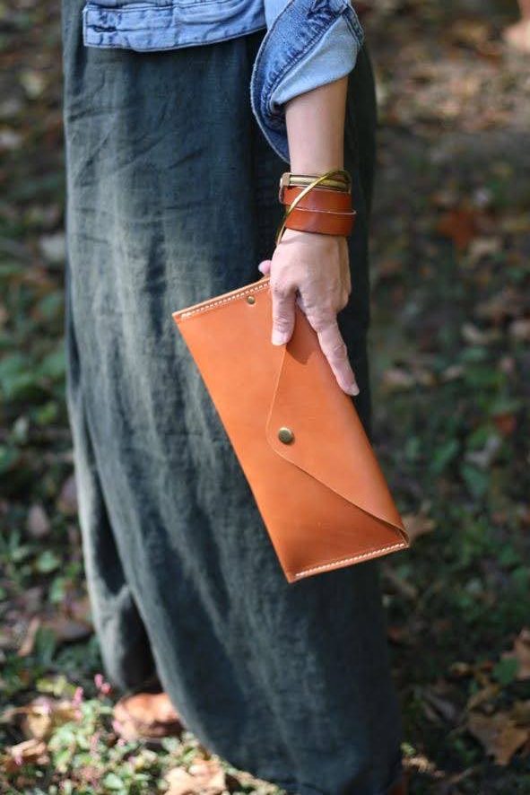 Wanderlust Leather Wristlet in Tan and cuff in Chestnut, held outside in the forest. Linen Skirt behind.